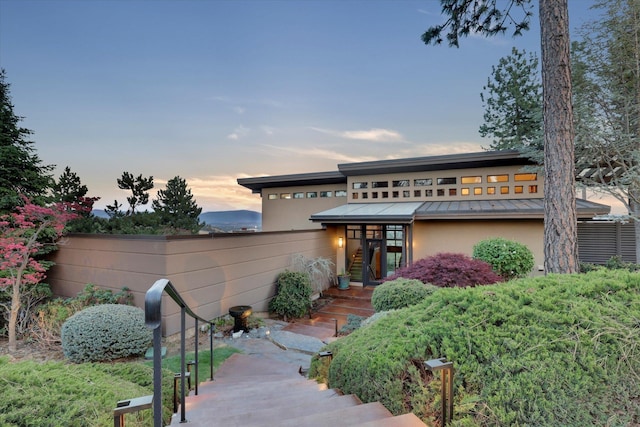 view of front of home with fence, stucco siding, stairway, metal roof, and a standing seam roof