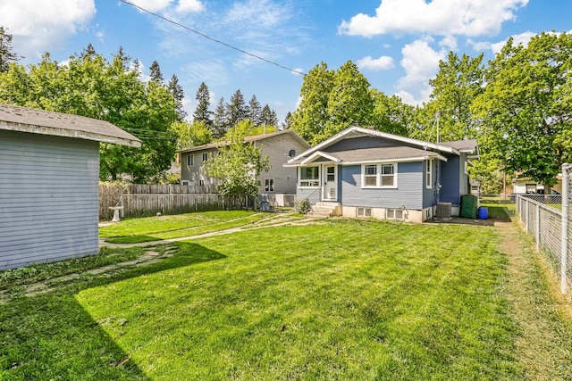 rear view of house featuring a yard, entry steps, a fenced backyard, and central AC