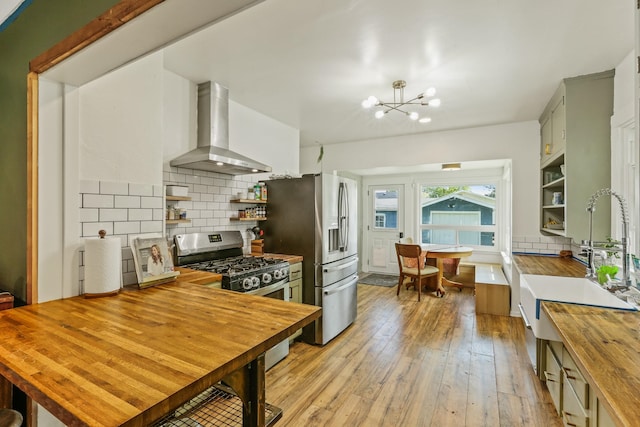 kitchen with open shelves, light wood-style floors, butcher block countertops, wall chimney range hood, and appliances with stainless steel finishes