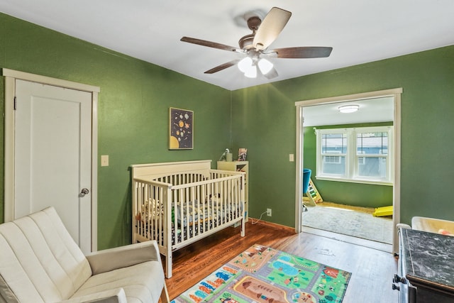 bedroom featuring baseboards, a ceiling fan, a crib, and wood finished floors