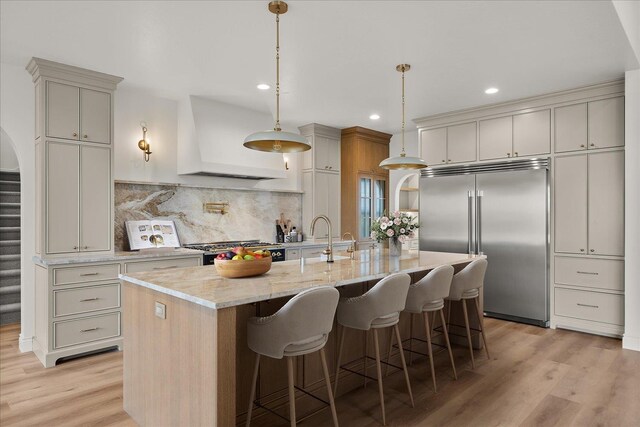 kitchen with built in fridge, wall chimney range hood, a sink, light wood-type flooring, and backsplash