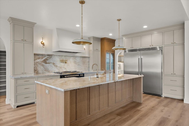 kitchen with stainless steel built in refrigerator, premium range hood, a sink, light wood-style flooring, and decorative backsplash