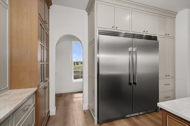kitchen featuring stainless steel built in refrigerator, light wood finished floors, light countertops, arched walkways, and baseboards