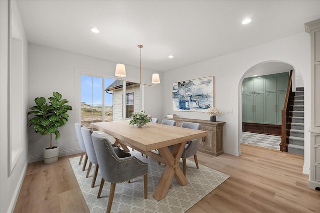 dining space featuring arched walkways, light wood-style flooring, baseboards, recessed lighting, and stairway