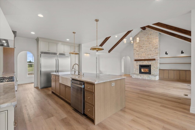 kitchen featuring arched walkways, a sink, stainless steel appliances, a kitchen island with sink, and light wood finished floors
