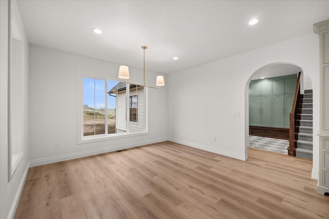 unfurnished dining area featuring arched walkways, light wood-style flooring, baseboards, recessed lighting, and stairway