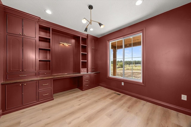 unfurnished office with light wood-style floors, a chandelier, built in desk, baseboards, and recessed lighting