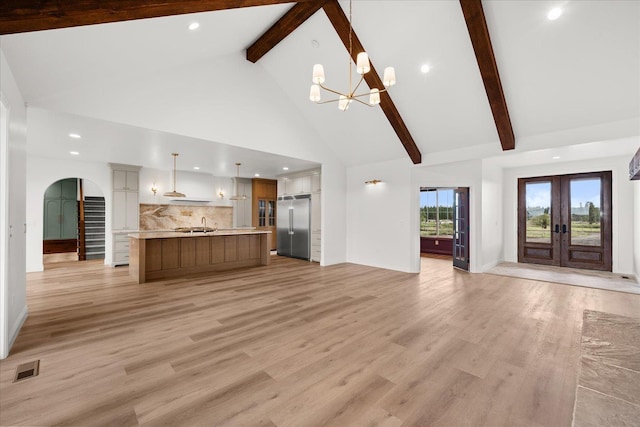 unfurnished living room with arched walkways, high vaulted ceiling, french doors, beamed ceiling, and a chandelier