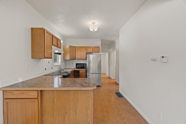 kitchen featuring a peninsula, a sink, freestanding refrigerator, a textured ceiling, and black microwave