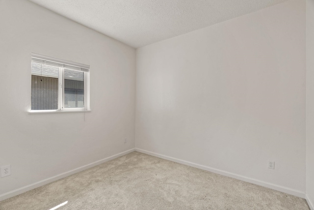 carpeted spare room featuring a textured ceiling and baseboards
