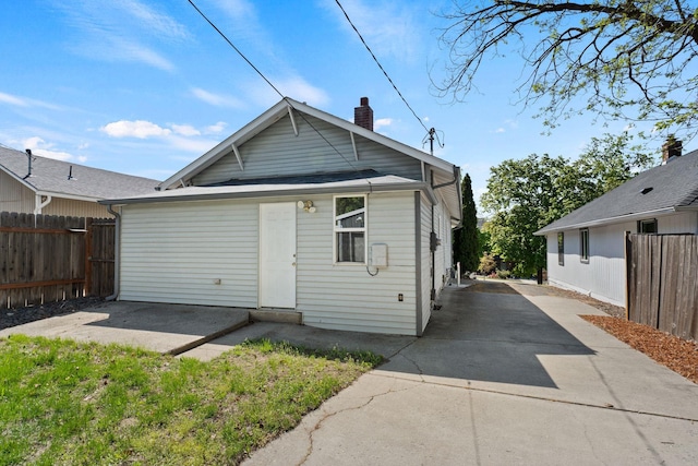 back of house with concrete driveway, a patio area, a chimney, and fence