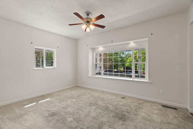 carpeted spare room featuring baseboards, ceiling fan, visible vents, and plenty of natural light
