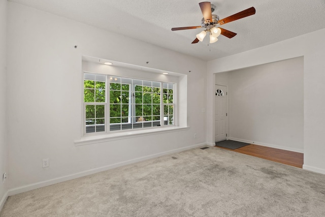 carpeted empty room with a textured ceiling, baseboards, a ceiling fan, and visible vents