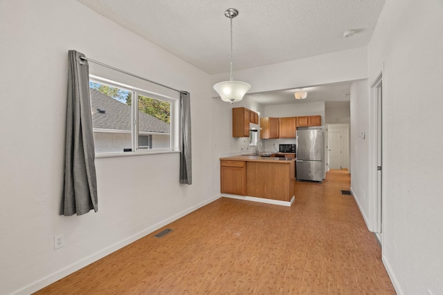 kitchen with a peninsula, brown cabinetry, freestanding refrigerator, light wood-type flooring, and baseboards