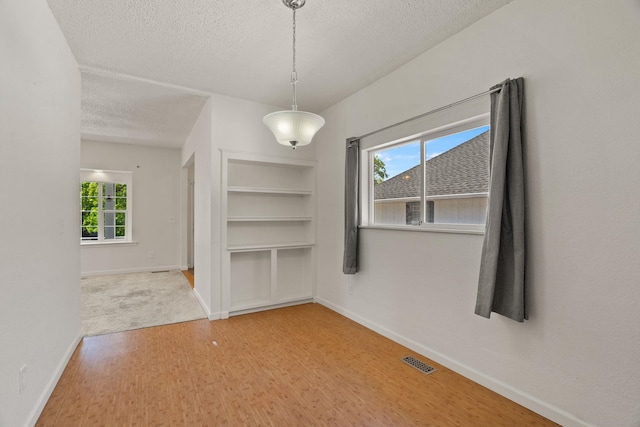 unfurnished dining area featuring wood finished floors, a textured ceiling, visible vents, built in shelves, and baseboards