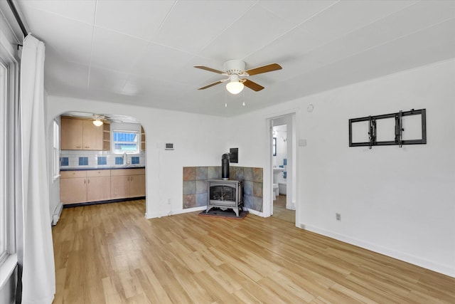 unfurnished living room with a wood stove, light wood finished floors, a ceiling fan, and a sink