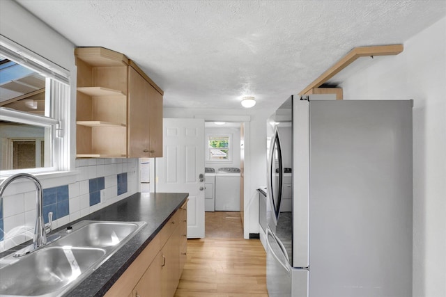 kitchen with washer and dryer, a sink, stainless steel fridge with ice dispenser, open shelves, and backsplash