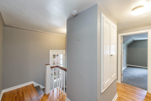corridor with baseboards, light wood-type flooring, and an upstairs landing