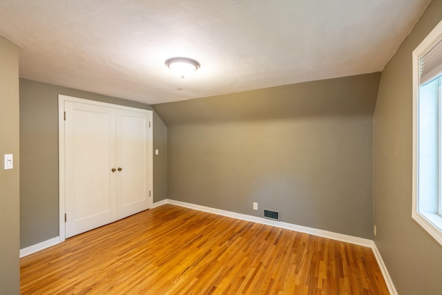 additional living space with light wood-type flooring, baseboards, visible vents, and lofted ceiling