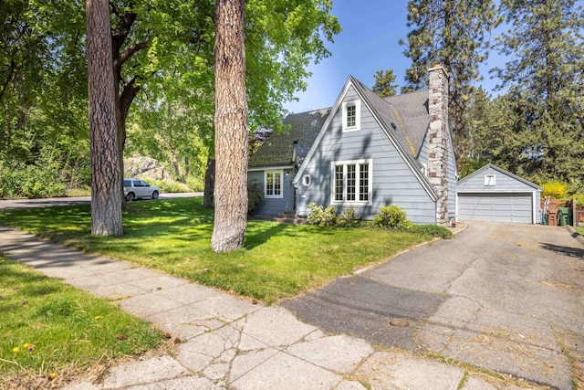 view of front facade with a chimney, an outbuilding, a garage, a shingled roof, and a front lawn