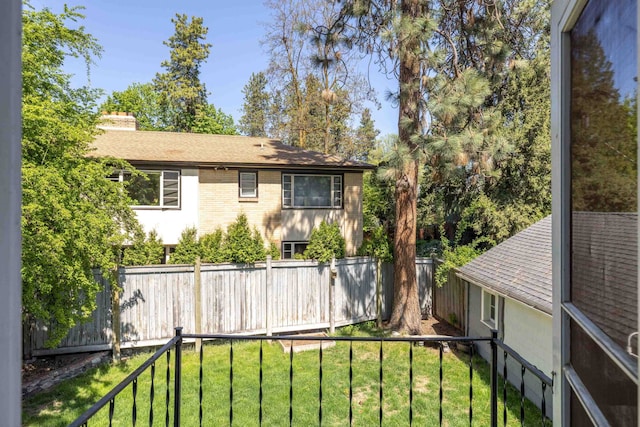 exterior space with brick siding, a fenced backyard, a chimney, a lawn, and a shingled roof