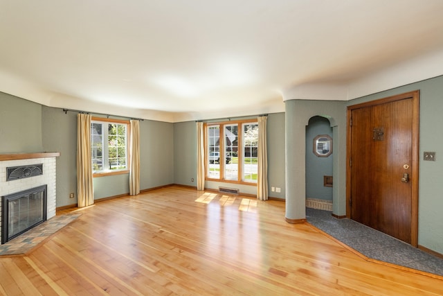 unfurnished living room featuring light wood-type flooring, visible vents, a brick fireplace, and arched walkways