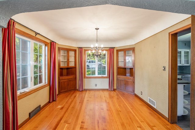 unfurnished dining area featuring an inviting chandelier, light wood-style flooring, baseboards, and visible vents