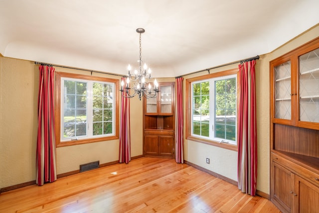 unfurnished dining area with visible vents, a chandelier, light wood-style flooring, a textured wall, and baseboards