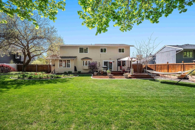 back of house with a lawn, a wooden deck, stucco siding, and a fenced backyard