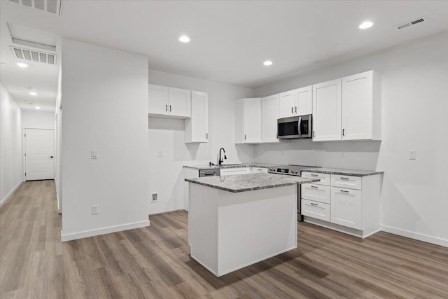 kitchen featuring white cabinets, appliances with stainless steel finishes, a center island, and wood finished floors
