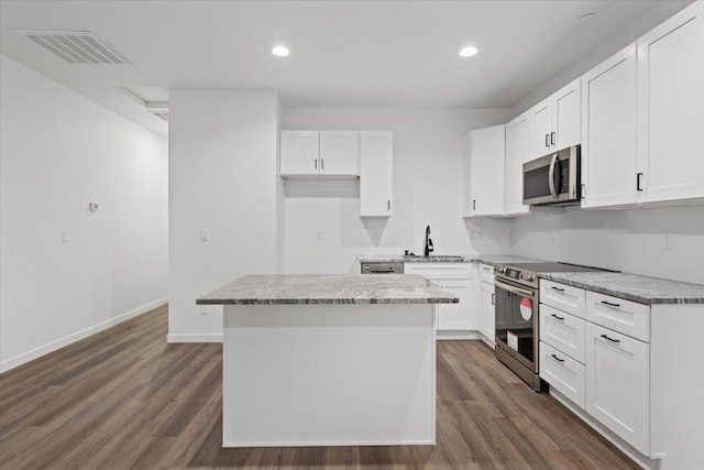 kitchen with dark wood finished floors, appliances with stainless steel finishes, a kitchen island, and a sink