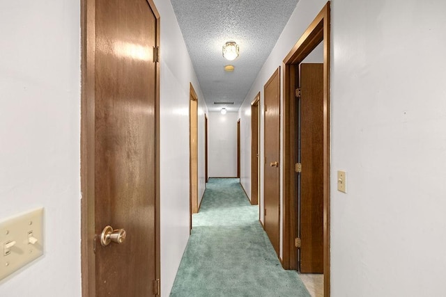corridor with light colored carpet and a textured ceiling