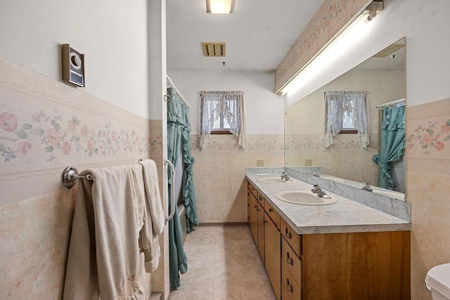 bathroom with tile walls, a wainscoted wall, double vanity, and a sink