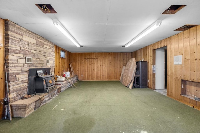 finished below grade area featuring a wood stove, carpet flooring, and wood walls