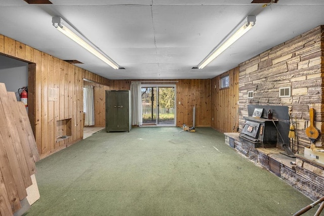 unfurnished living room featuring a wood stove, wooden walls, light colored carpet, and visible vents