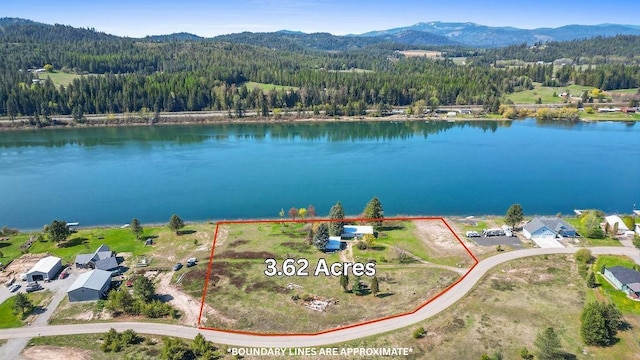 aerial view featuring a water and mountain view and a view of trees