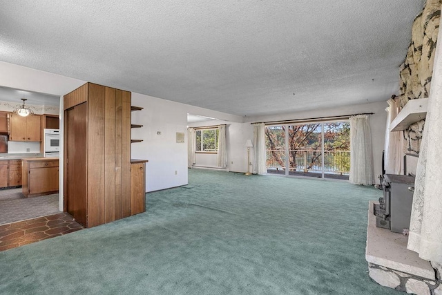unfurnished living room featuring a textured ceiling, a wealth of natural light, a wood stove, and carpet