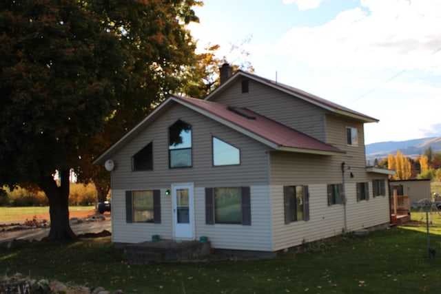 rear view of property featuring a mountain view, a chimney, and a lawn