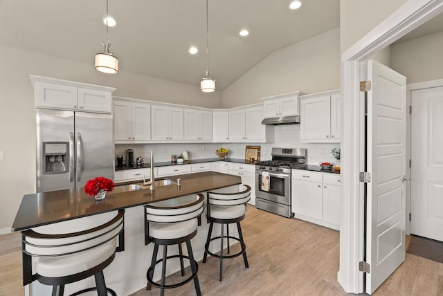 kitchen featuring dark countertops, stainless steel appliances, under cabinet range hood, and vaulted ceiling