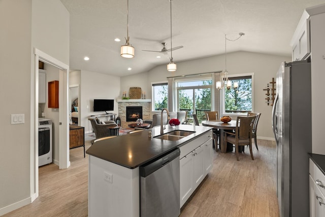 kitchen with a sink, vaulted ceiling, dark countertops, stainless steel appliances, and light wood-type flooring