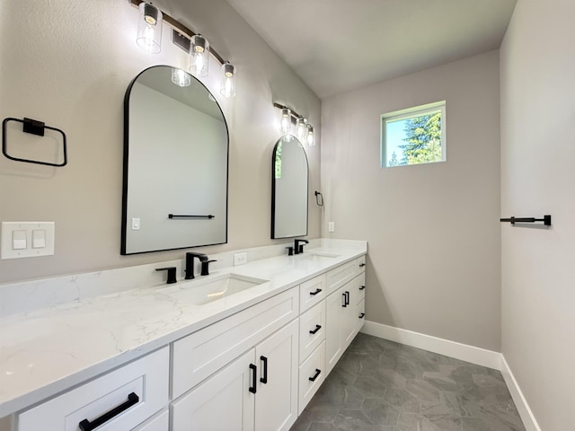 full bath featuring baseboards, marble finish floor, double vanity, and a sink