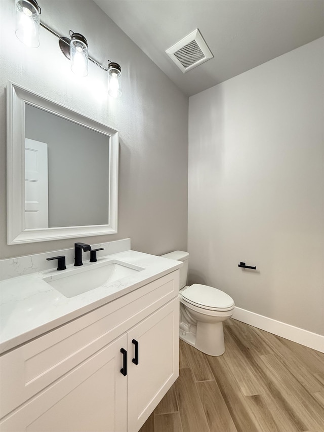bathroom with toilet, wood finished floors, vanity, visible vents, and baseboards
