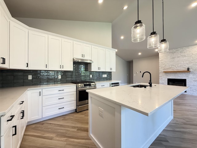 kitchen with under cabinet range hood, a sink, gas range, backsplash, and a center island with sink