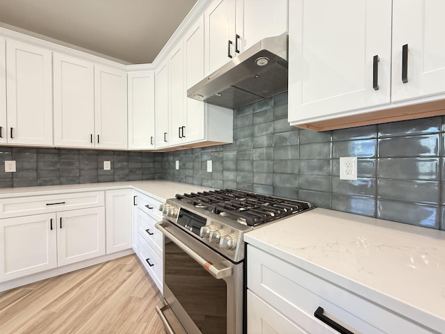 kitchen featuring under cabinet range hood, stainless steel gas stove, white cabinetry, backsplash, and light wood-style floors