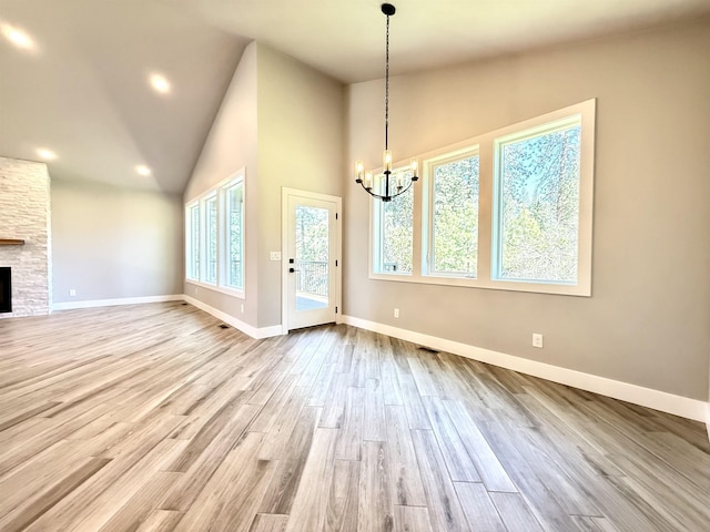 unfurnished dining area featuring baseboards, a stone fireplace, a chandelier, and wood finished floors