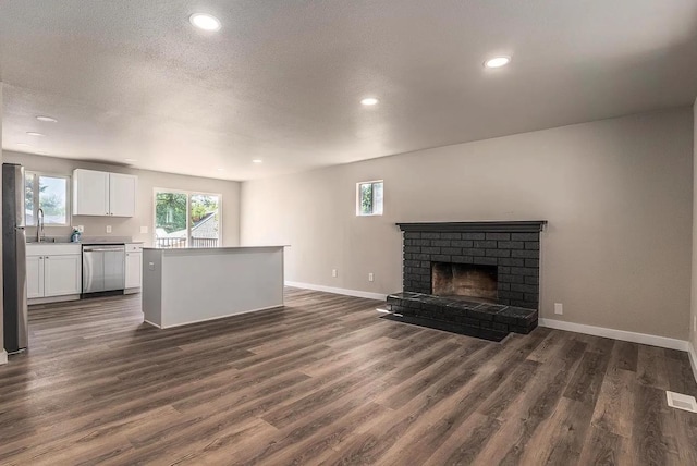 unfurnished living room featuring recessed lighting, baseboards, a sink, a brick fireplace, and dark wood-type flooring