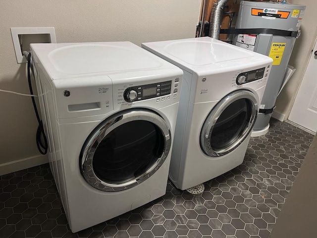 clothes washing area featuring washing machine and clothes dryer, laundry area, dark tile patterned flooring, baseboards, and electric water heater