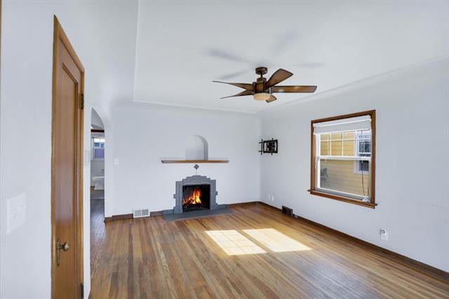 2424 W Fairview Ave, Spokane, WA 99205 - unfurnished living room with wood finished floors, a warm lit fireplace, a ceiling fan, arched walkways, and baseboards