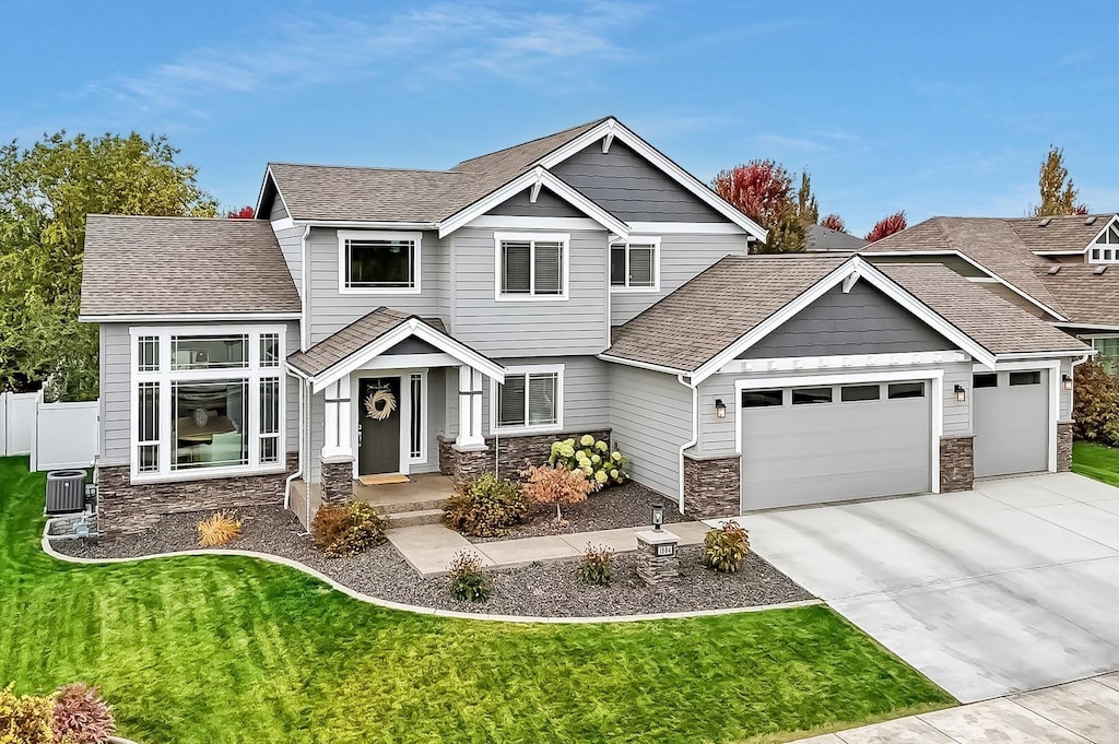 craftsman-style house featuring stone siding, a garage, driveway, and a shingled roof