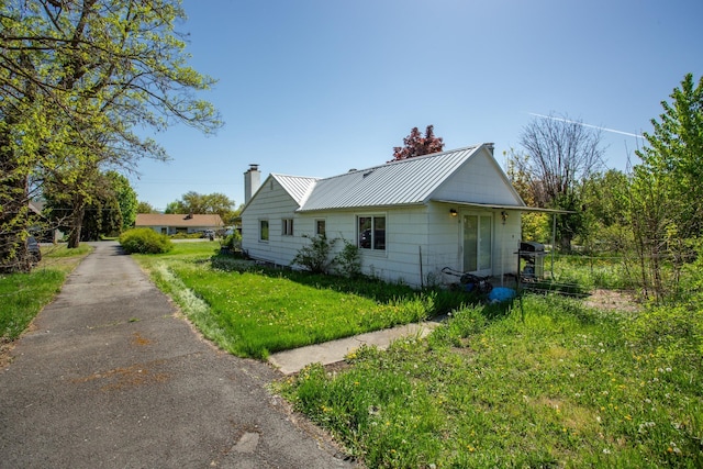 view of side of property featuring metal roof, a yard, and a chimney